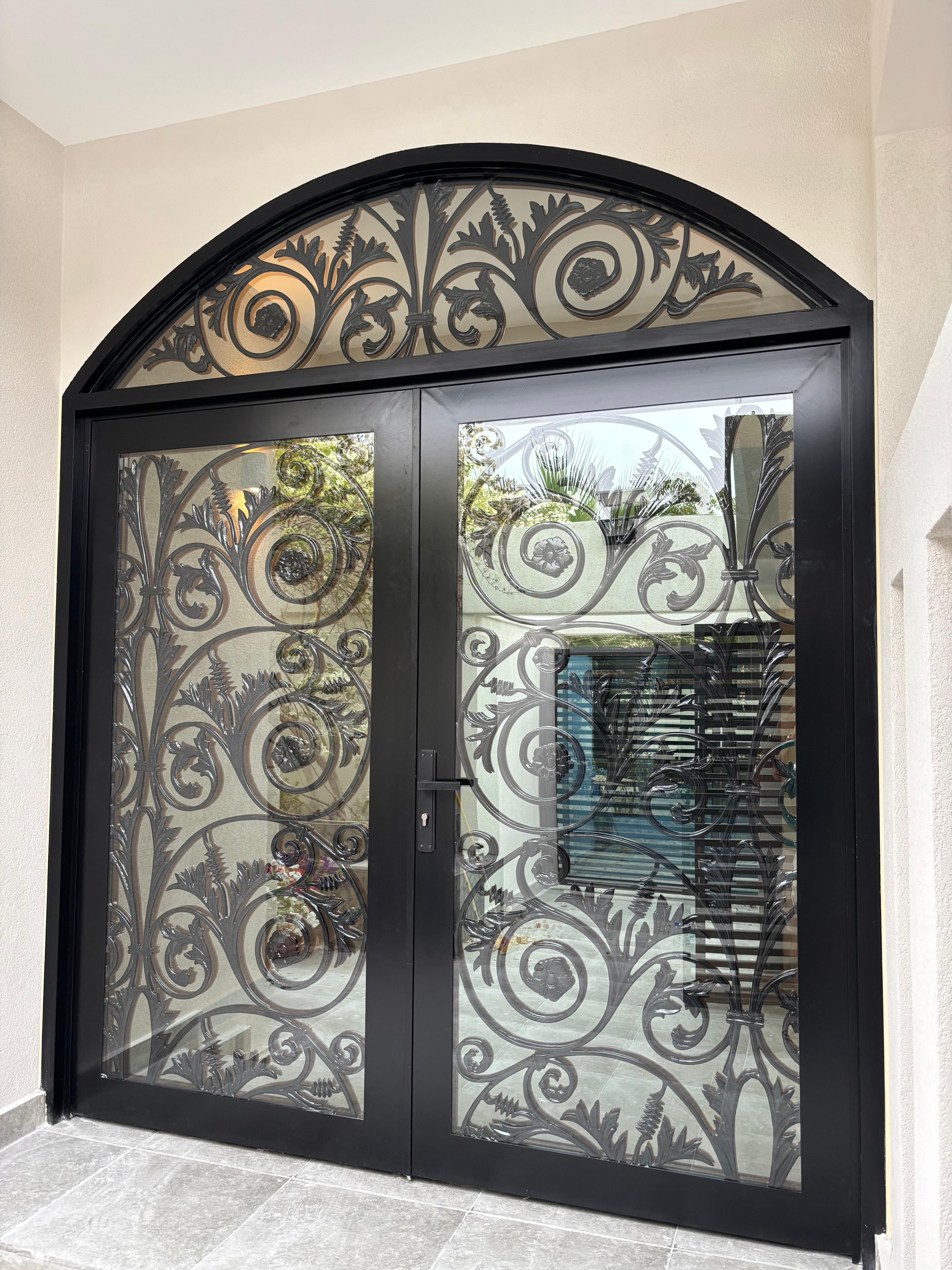 Black-framed double doors with arched transom and decorative metal scrollwork over clear glass
